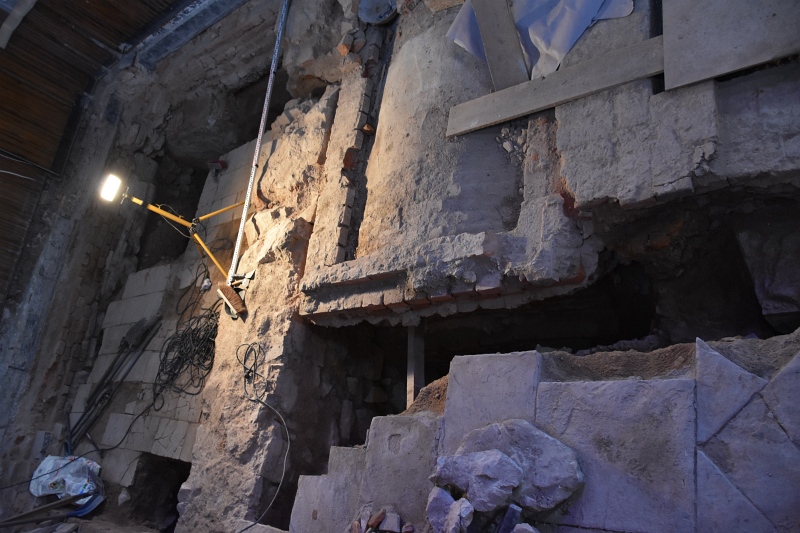 Fotografia wnętrza remontowanej kaplicy z widocznymi wykopami badawczymi oraz odsłoniętymi fragmentami murów kamiennych i krypt.